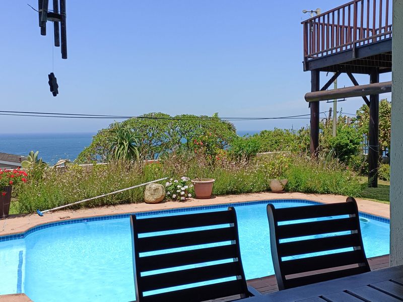 Outdoor pool area featuring a swimming pool with tiled surround, overlooking the ocean with a raised wooden deck structure above.