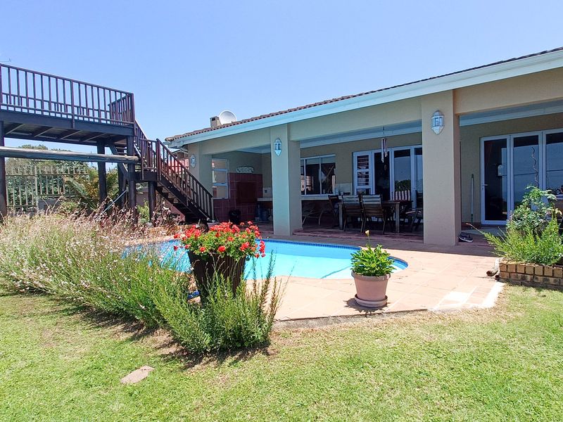 Outdoor entertainment area featuring a swimming pool, covered patio with built-in braai, and a raised wooden viewing deck overlooking the garden.