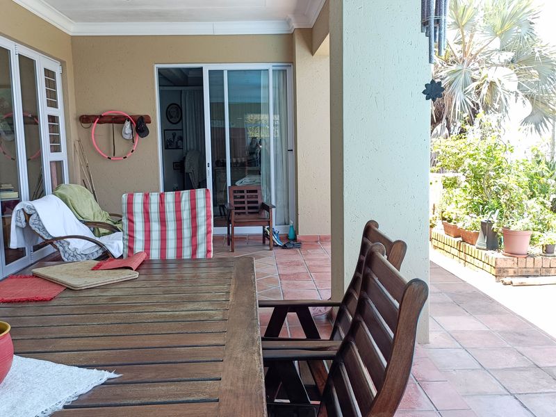 A covered patio area featuring tiled flooring and sliding glass doors, providing a seamless transition to the outdoor garden space.