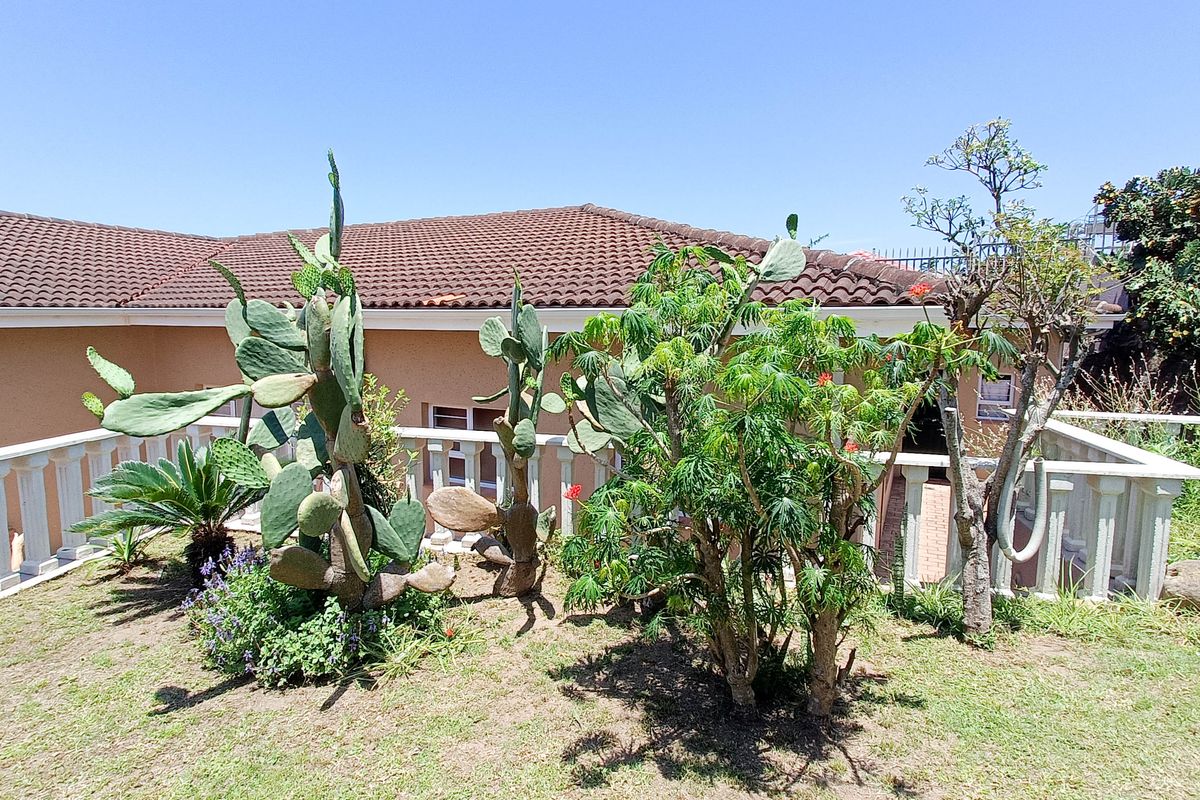 Rear exterior view of the property featuring a tiled roof, stucco walls, and a decorative balustrade overlooking a landscaped garden area.