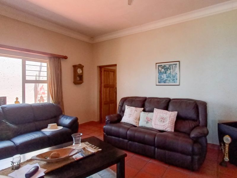 A comfortable living room featuring terracotta floor tiles, coved ceilings, and natural light through a large window.