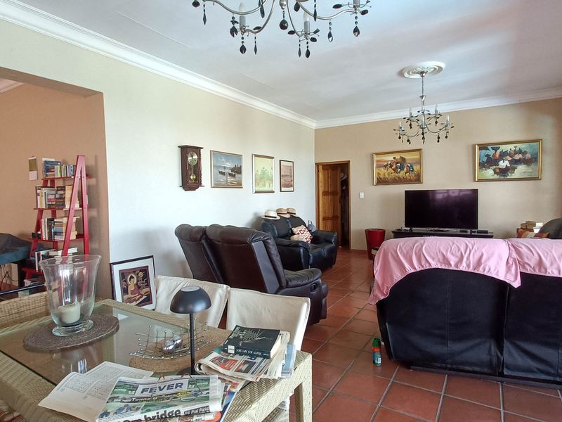 Spacious open-plan living and dining area featuring terracotta floor tiles, decorative ceiling roses with chandeliers, and access to an outdoor space via sliding doors.