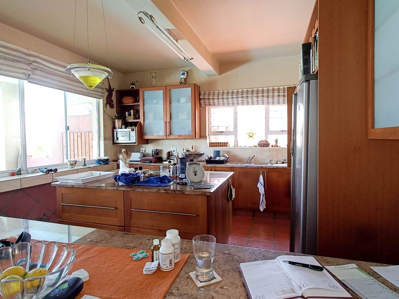 A functional kitchen featuring wooden cabinetry, granite countertops, and a central island, offering ample workspace and natural light through large windows.