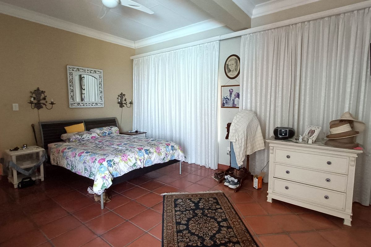 Spacious bedroom featuring terracotta floor tiles, crown molding, and a ceiling fan, offering a neutral base for potential interior updates.