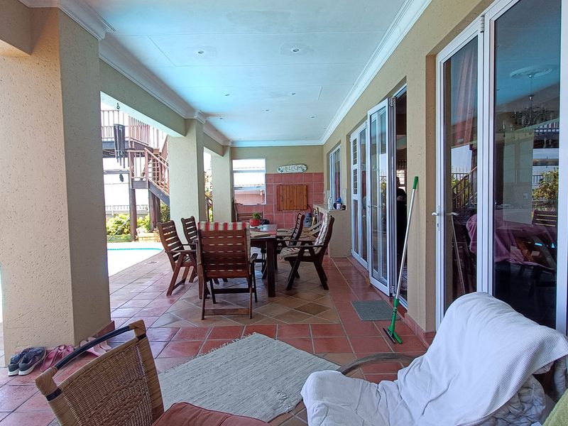 A spacious covered patio featuring tiled flooring, recessed lighting, and multiple sliding glass doors providing access to the interior and pool area.