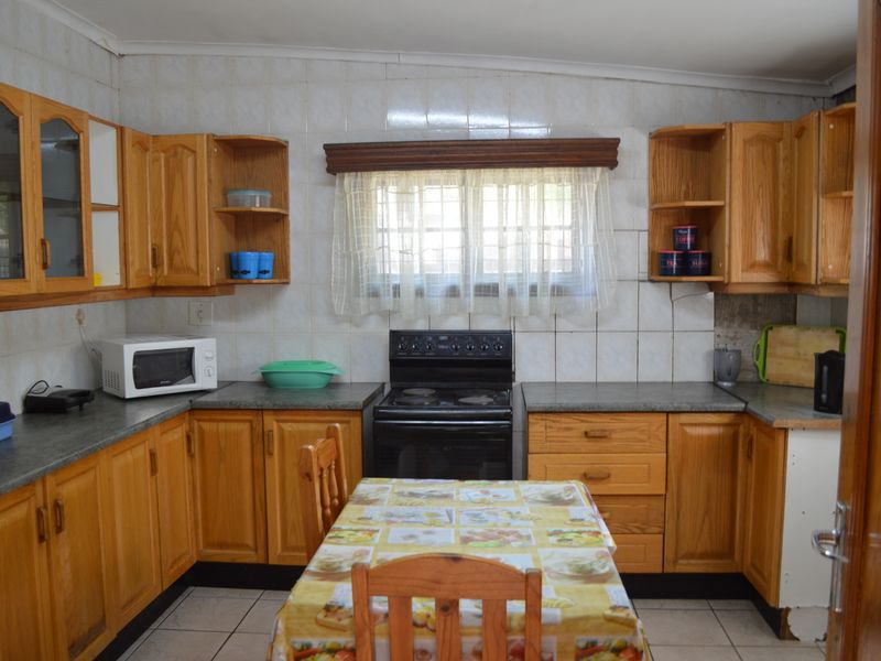 A dated kitchen featuring wooden cabinetry, tiled backsplash, and a freestanding electric stove, offering a functional layout with potential for modern updates.