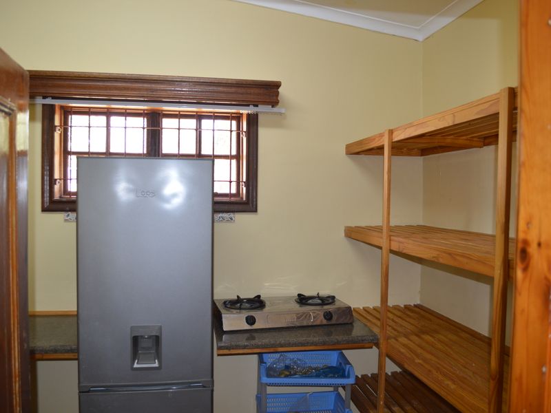 A functional scullery or utility area featuring stone countertops, built-in wooden shelving, and a window with security bars.