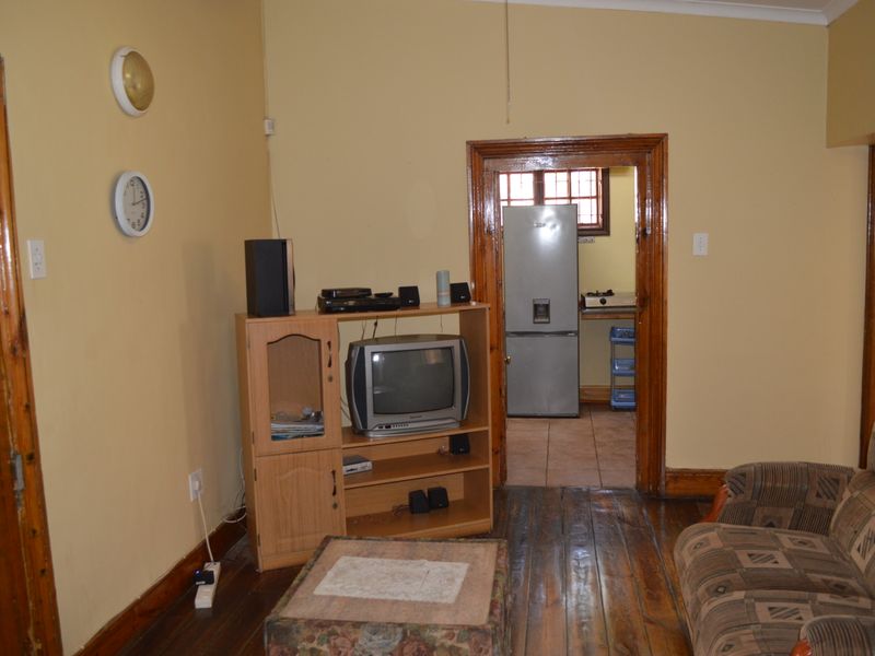 A living room featuring original timber flooring and traditional timber door frames, leading through to a kitchen area.