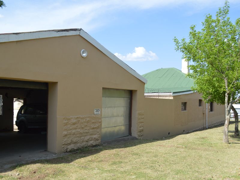 A detached garage structure with a metal door and adjacent perimeter wall featuring security razor wire, set on a grassed lot.