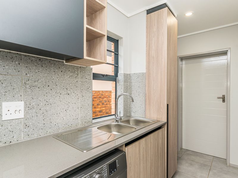 A modern, well-maintained scullery featuring a double bowl stainless steel sink, terrazzo-style splashback, and contemporary wood-look cabinetry with ample storage.
