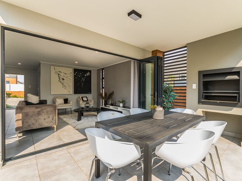 Covered patio featuring a built-in braai, tiled flooring, and large sliding doors that provide seamless access to the indoor living area.