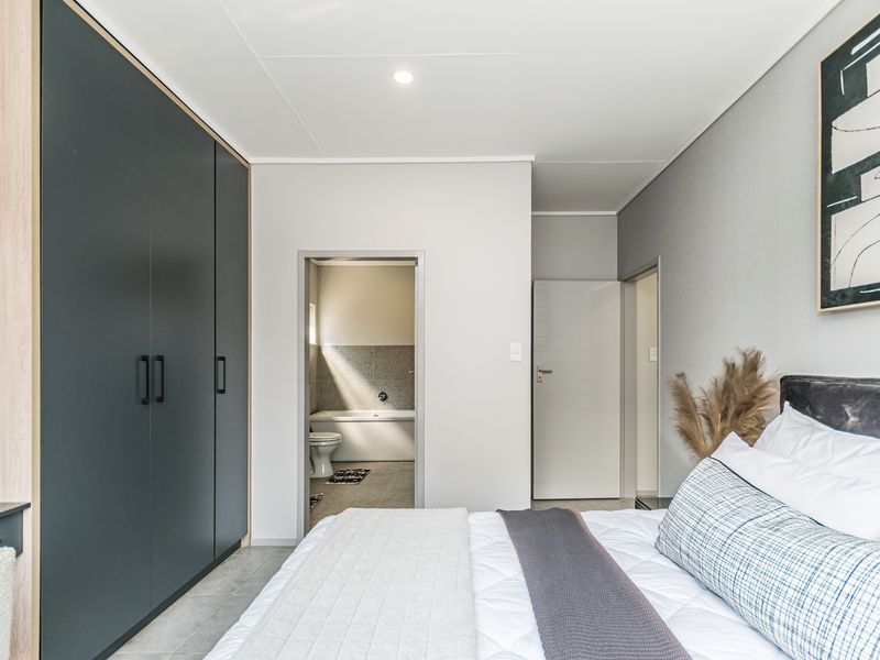 Modern bedroom featuring built-in cupboards, neutral finishes, and direct access to an en-suite bathroom with a bathtub.