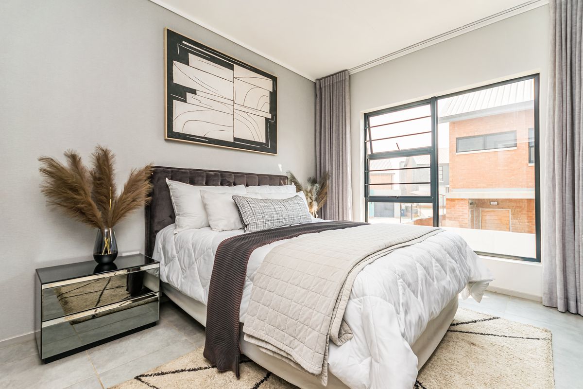 A well-maintained bedroom featuring neutral wall tones, tiled flooring, and large aluminium-framed windows allowing for ample natural light.