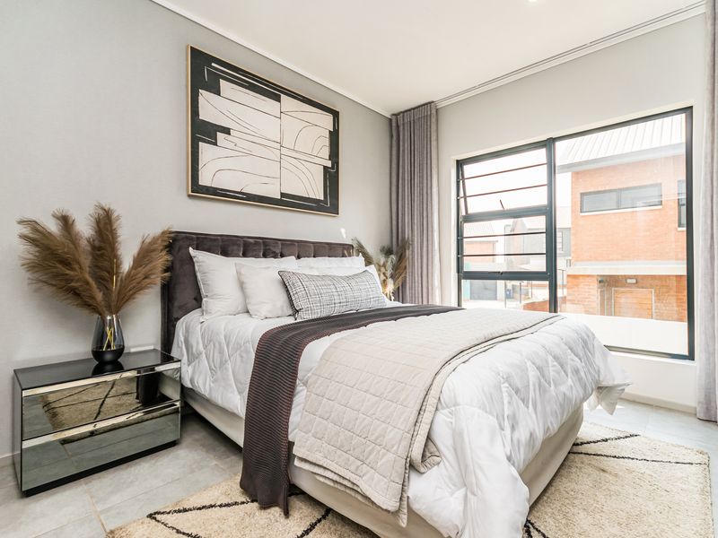 A well-maintained bedroom featuring neutral wall tones, tiled flooring, and large aluminium-framed windows allowing for ample natural light.