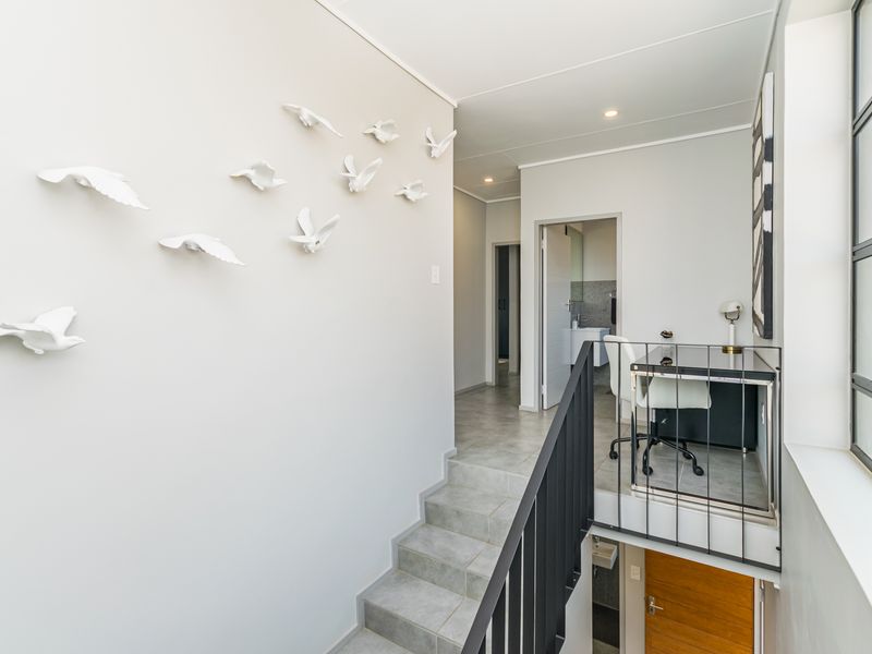A bright, modern hallway featuring tiled flooring, a sleek metal staircase railing, and large steel-framed windows that allow for ample natural light.