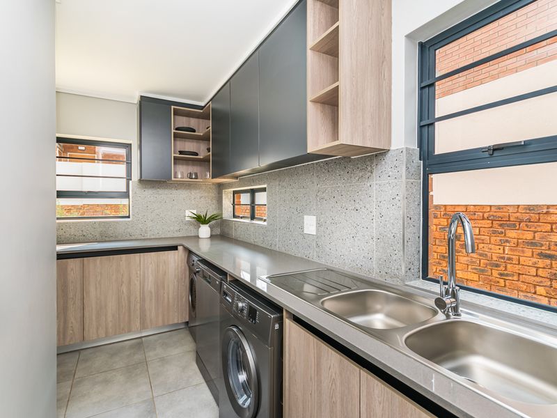 Modern scullery featuring sleek two-tone cabinetry, terrazzo-style tiled splashbacks, double stainless steel sink, and integrated space for laundry appliances.
