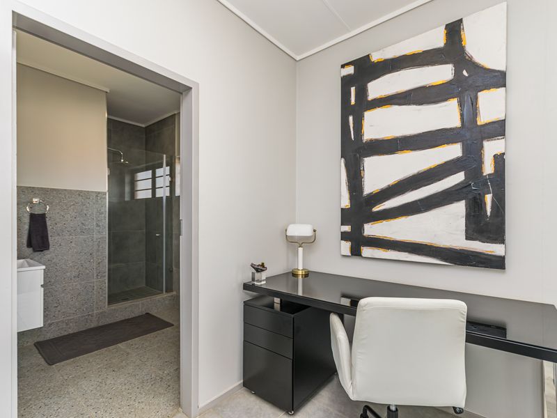 A functional home office space featuring a built-in desk, with direct access to an en-suite bathroom equipped with a modern shower and vanity.