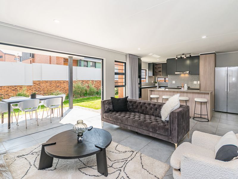 Modern open-plan living area featuring a sleek kitchen with island, tiled floors, and seamless flow to the outdoor patio through large sliding glass doors.