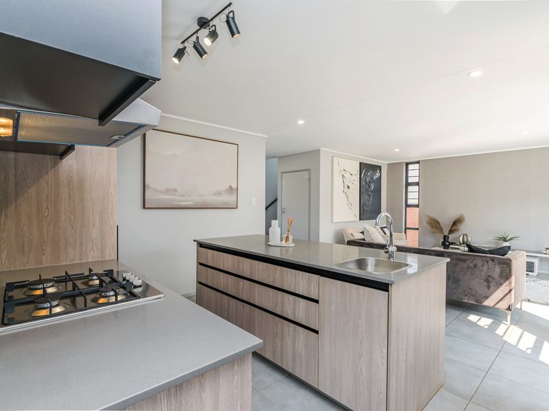 Modern open-plan kitchen featuring a central island with stone countertops, gas hob, extractor fan, and sleek cabinetry, flowing into the living area.