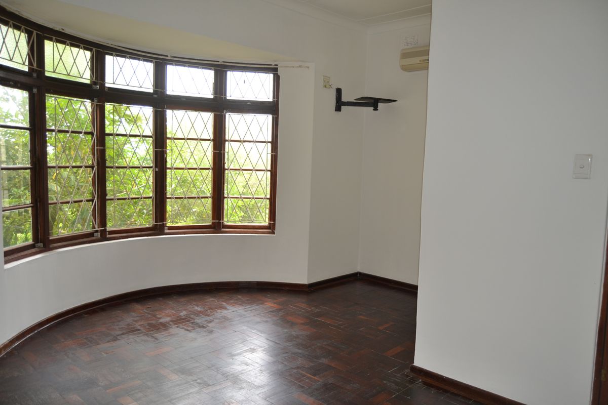 A bright bedroom featuring classic bay windows, dark parquet flooring, and a wall-mounted air conditioning unit.
