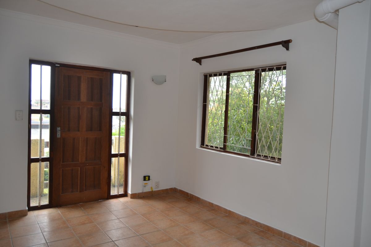 An empty living area featuring tiled flooring, a solid timber entrance door with side panels, and security-fitted windows.