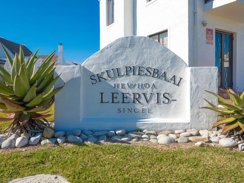 A well-maintained masonry signage structure at the entrance of the property, featuring landscaped garden beds and clear street-level identification.