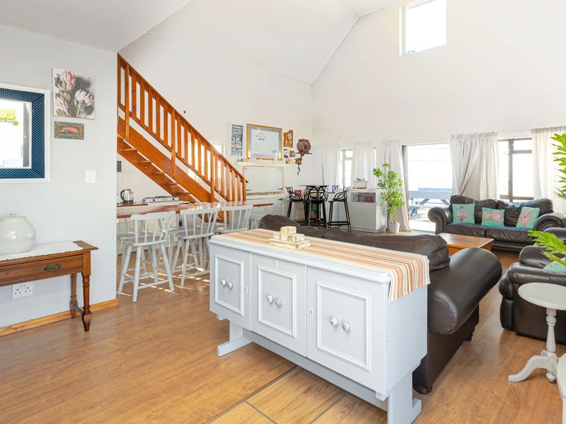 Spacious open-plan living area featuring a vaulted ceiling, laminate flooring, a wooden staircase, and a breakfast bar with direct access to outdoor space.