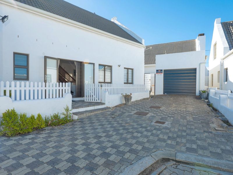 Front elevation of a white house featuring a paved driveway, garage, and a charming white picket fence entrance.