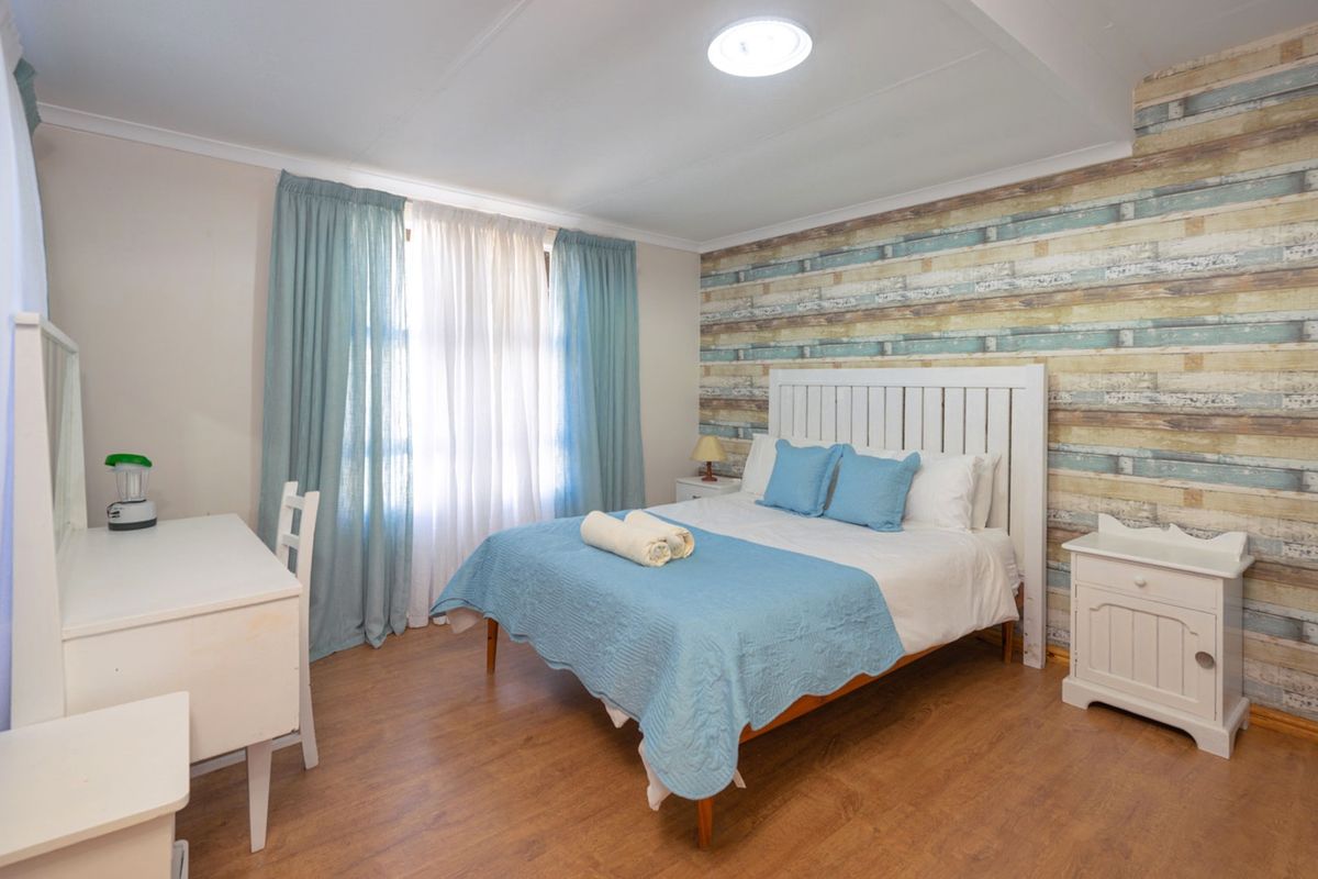A well-lit bedroom featuring laminate flooring and a decorative feature wall, offering a comfortable and functional living space.