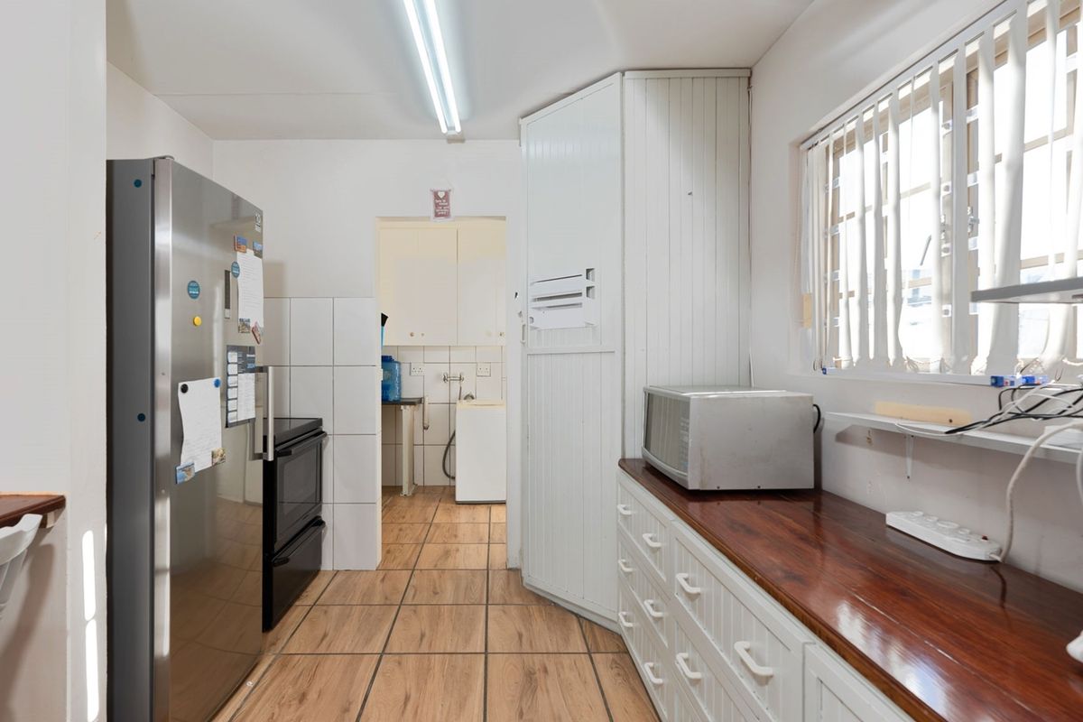 A functional kitchen featuring wooden countertops, tiled flooring, and built-in cabinetry, with an adjacent scullery area visible through the doorway.