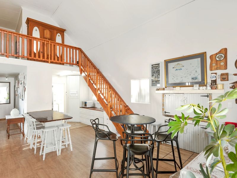 Open-plan living area featuring a vaulted ceiling, laminate flooring, and a wooden staircase leading to a mezzanine level with built-in cabinetry.