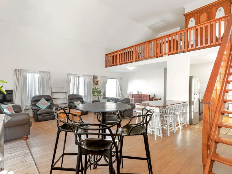 Spacious open-plan living and dining area featuring a vaulted ceiling, wooden staircase, and a mezzanine loft level with a wooden balustrade.