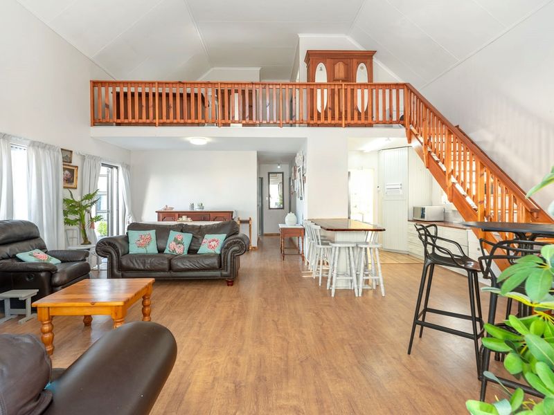 Spacious open-plan living area featuring a vaulted ceiling, mezzanine level with wooden balustrade, and integrated kitchen space with laminate flooring.