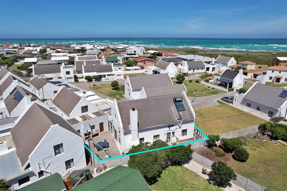 Aerial view of a coastal residential property featuring a white exterior, tiled roof with solar water heater, and a private paved patio area.