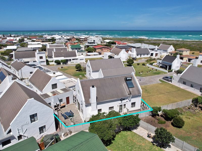 Aerial view of a coastal residential property featuring a white exterior, tiled roof with solar water heater, and a private paved patio area.