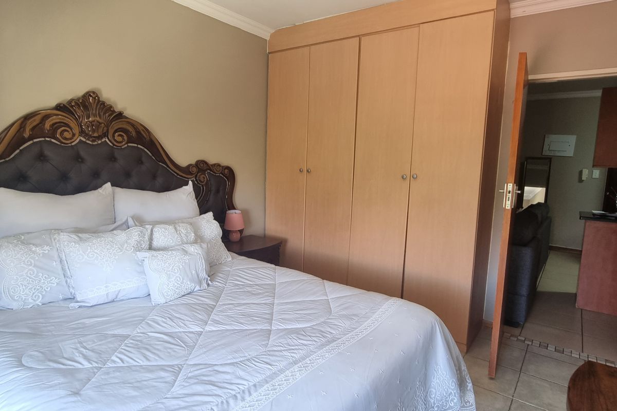 A bedroom featuring built-in wooden wardrobes, tiled flooring, and coving, with an open doorway leading to the adjacent living area.