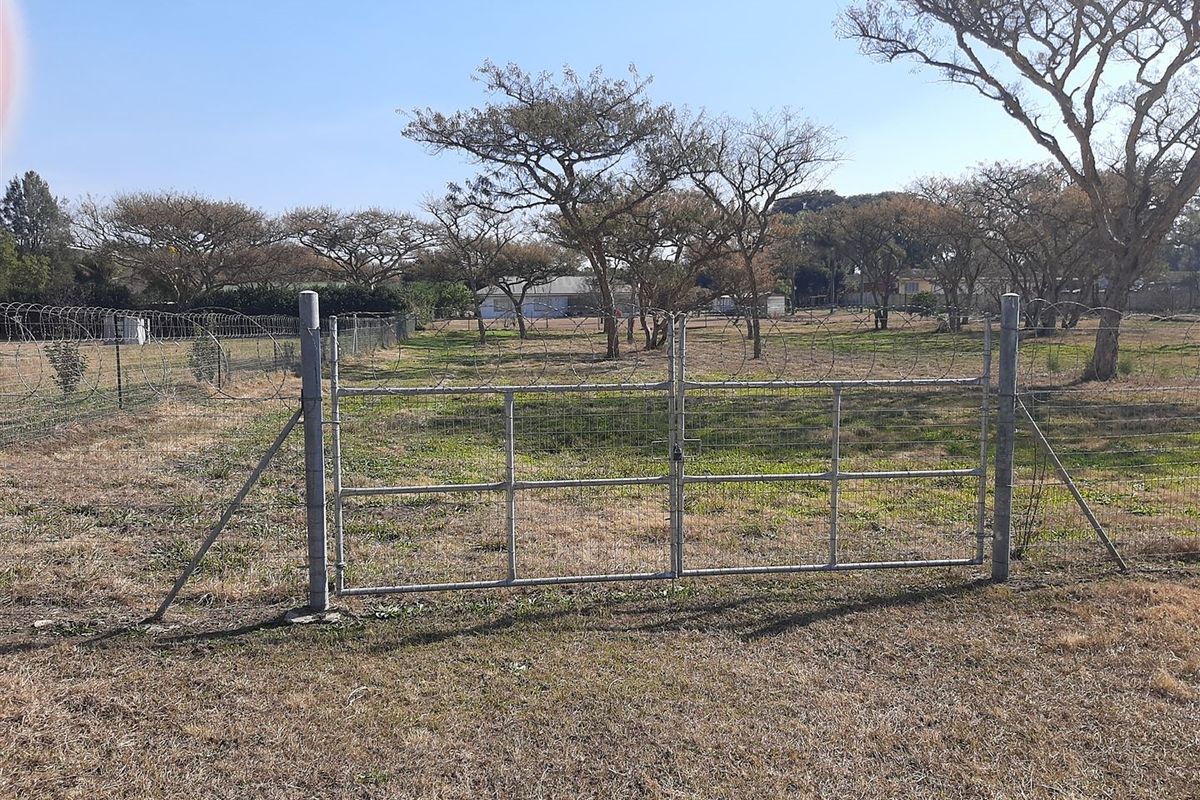 A view of a vacant residential plot featuring a metal gate entrance and perimeter wire fencing with razor wire.