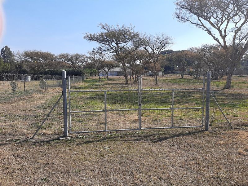 A view of a vacant residential plot featuring a metal gate entrance and perimeter wire fencing with razor wire.