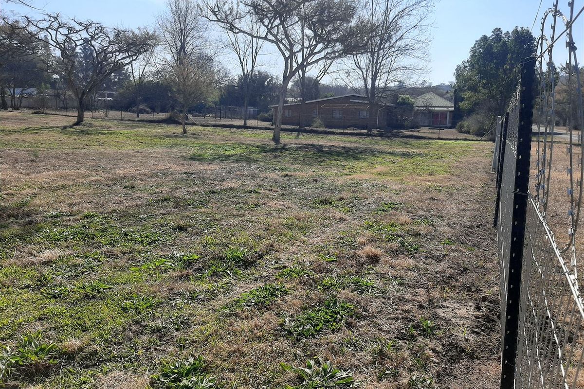 A view of a vacant residential plot featuring established trees and perimeter fencing with razor wire.