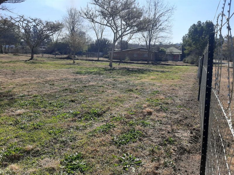A view of a vacant residential plot featuring established trees and perimeter fencing with razor wire.