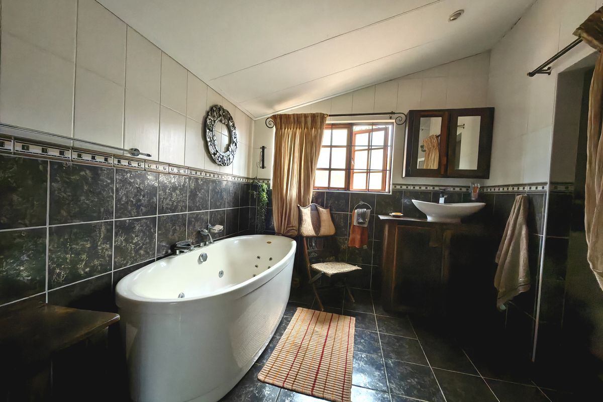 A bathroom featuring a freestanding jetted bathtub, a vessel sink with a vanity cabinet, and dark tiled finishes.