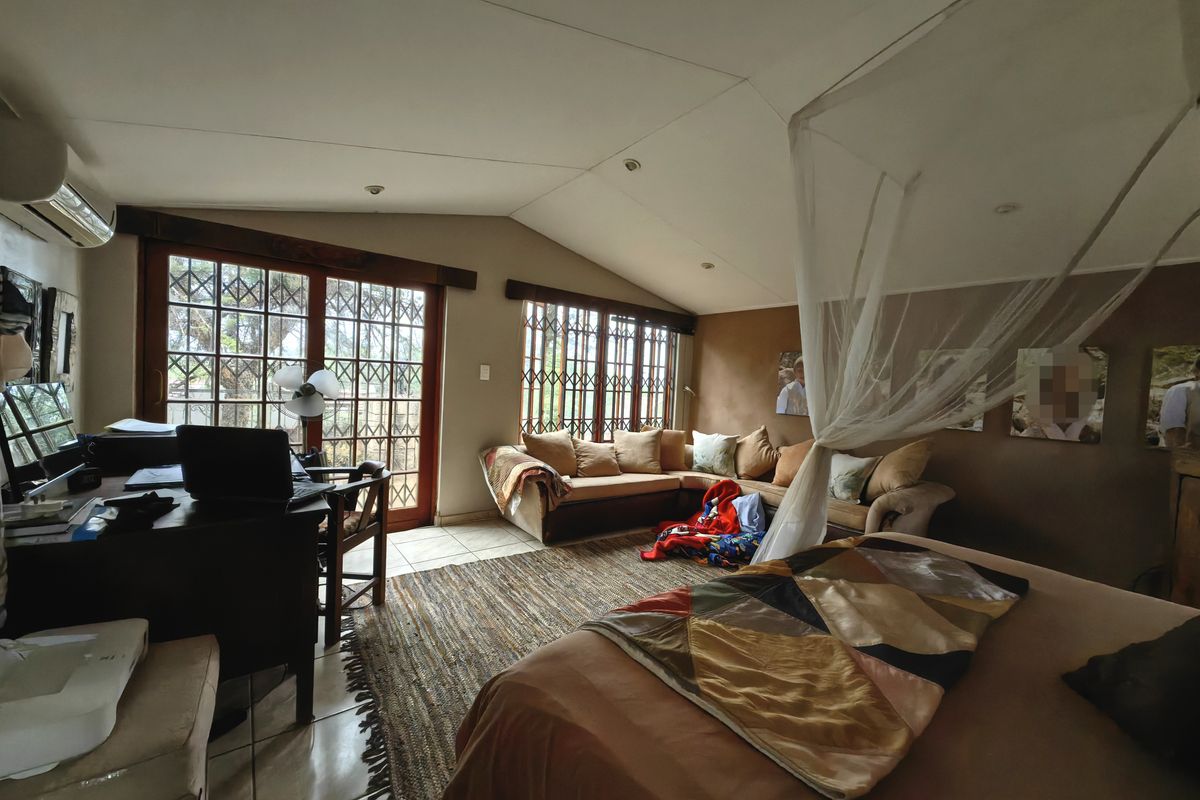Spacious bedroom featuring vaulted ceilings, tiled flooring, and large sliding glass doors with security gates, providing ample natural light and outdoor access.