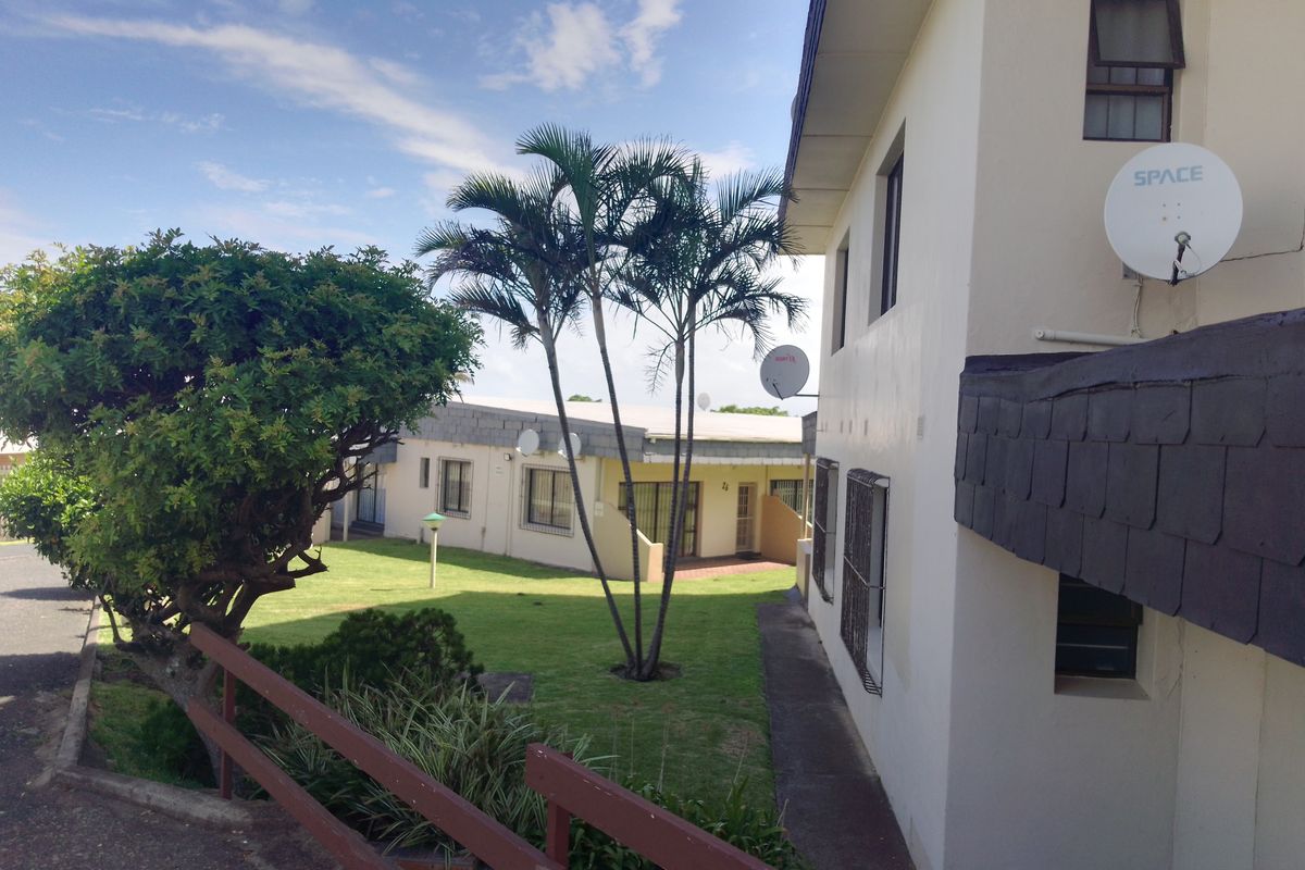 Exterior view of the apartment complex featuring a shared garden area, paved walkways, and residential building facades with satellite dishes.