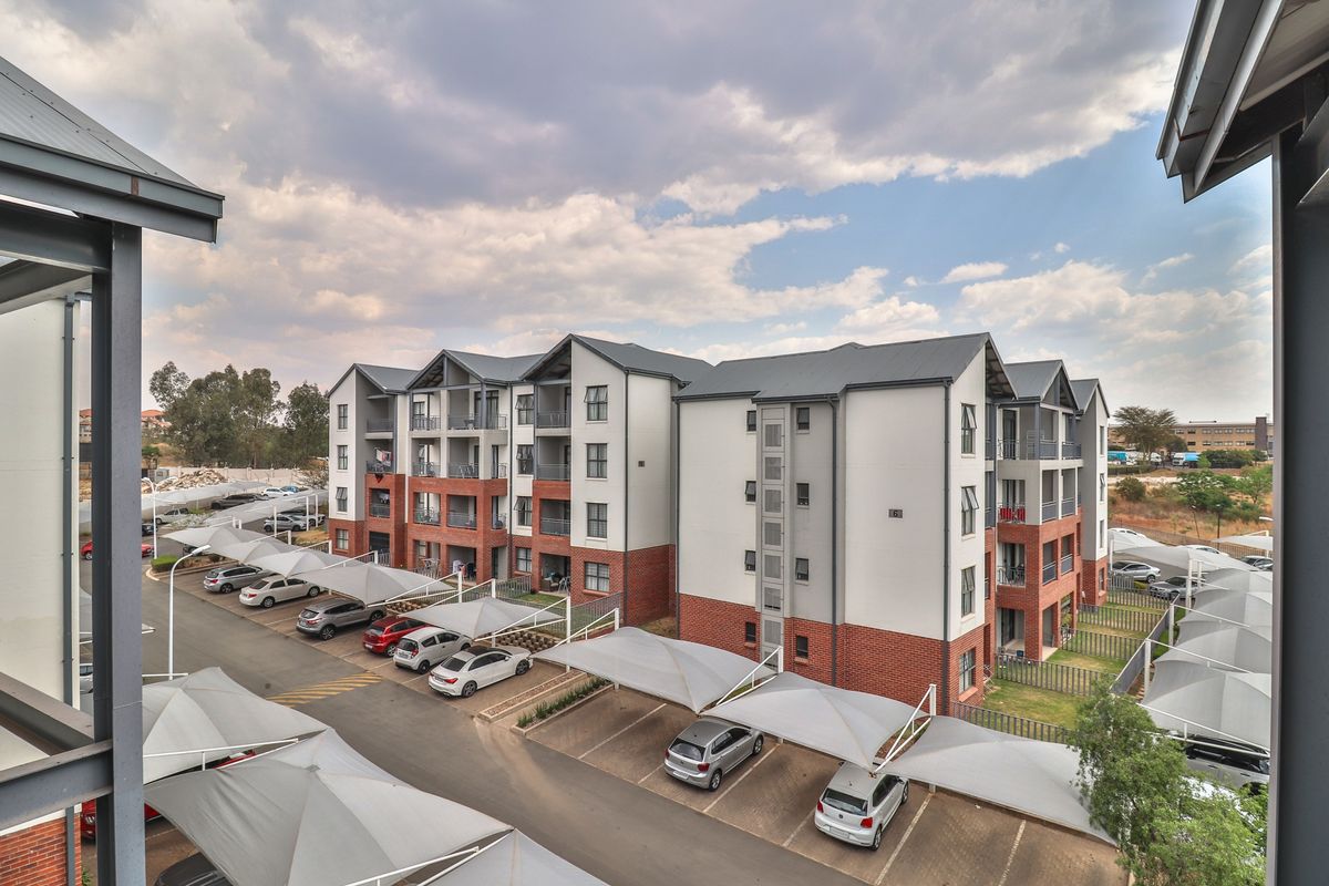 An elevated view of a modern apartment complex featuring brick and plaster facades, metal roofing, and designated covered parking areas.