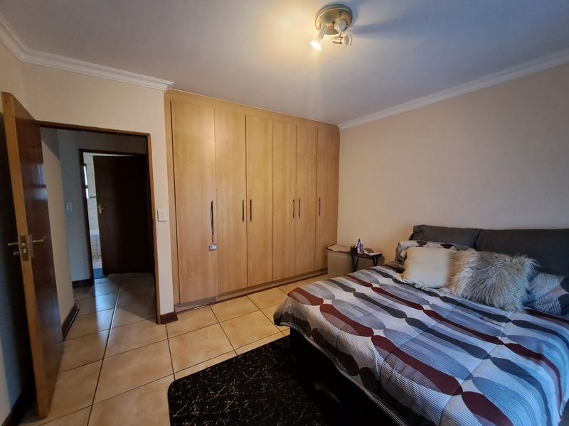 A bedroom featuring built-in wooden cupboards, tiled flooring, and a ceiling light fixture, with an adjacent hallway leading to another room.