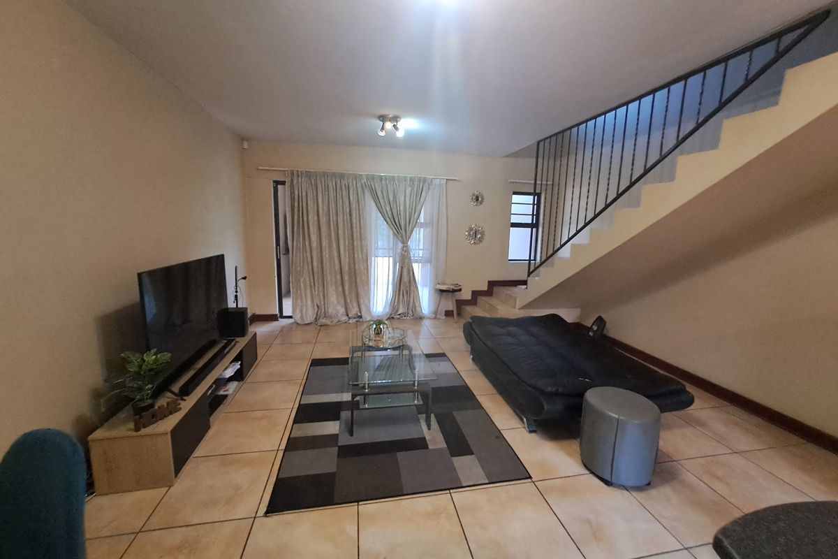 Spacious living room featuring tiled flooring, a staircase with a metal balustrade, and access to an outdoor area through sliding glass doors.