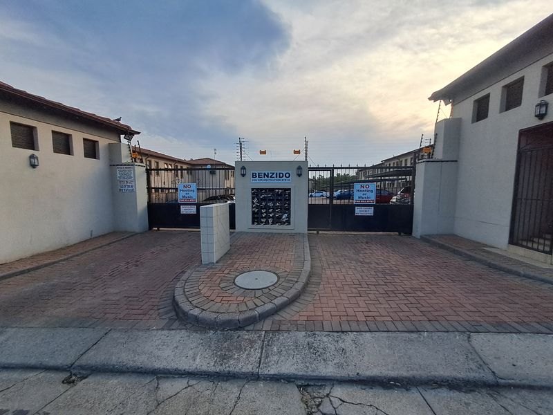 The entrance to the Benzido apartment complex featuring a secure gated access point, paved driveway, and integrated post boxes.