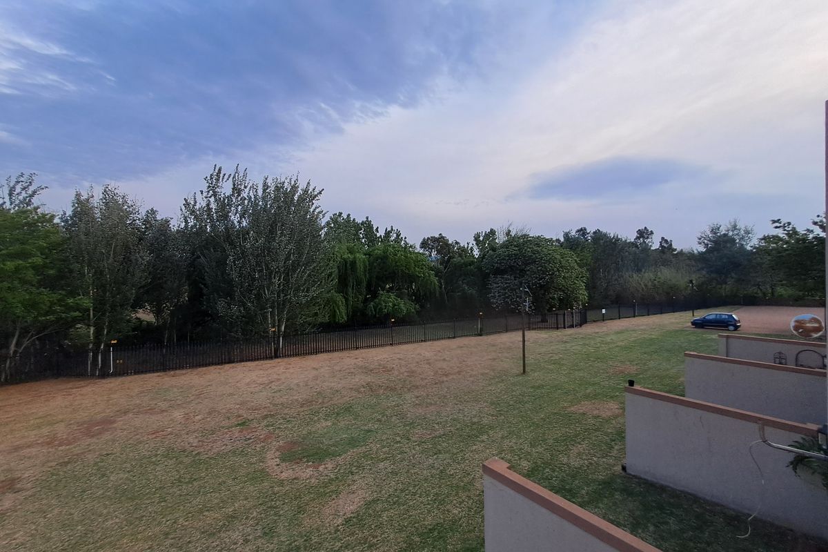 A view of the rear communal garden area featuring a lawn, perimeter fencing, and balcony partitions of the apartment complex.