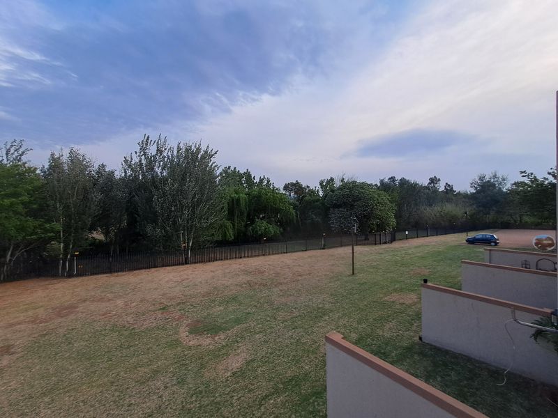 A view of the rear communal garden area featuring a lawn, perimeter fencing, and balcony partitions of the apartment complex.