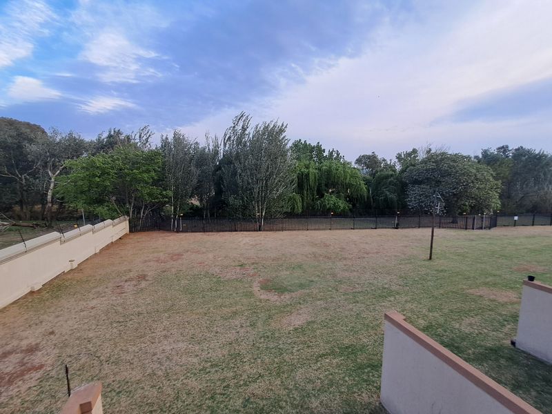 A spacious backyard area featuring a large lawn, enclosed by a perimeter wall and metal fencing with mature trees in the background.